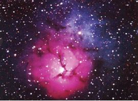 The Trifid Nebula in the constellation Sagittarius.  Red light comes from hydrogen gas atoms excited by the light from stars within the nebula; blue light from these stars is re-flected off fine dust particles back into our line of sight